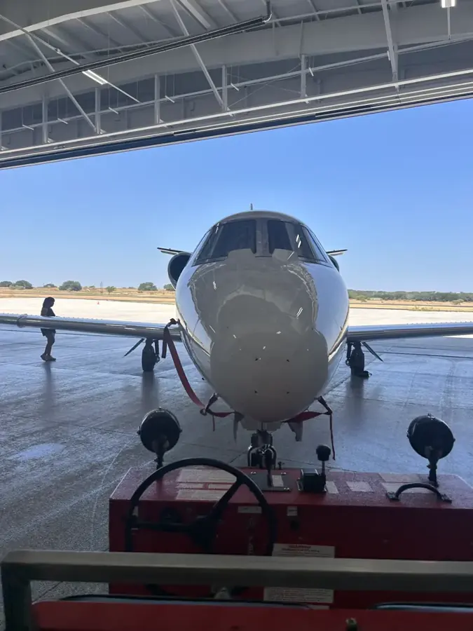 A light business jet on the ramp in a hangar doorway, seen nose on.