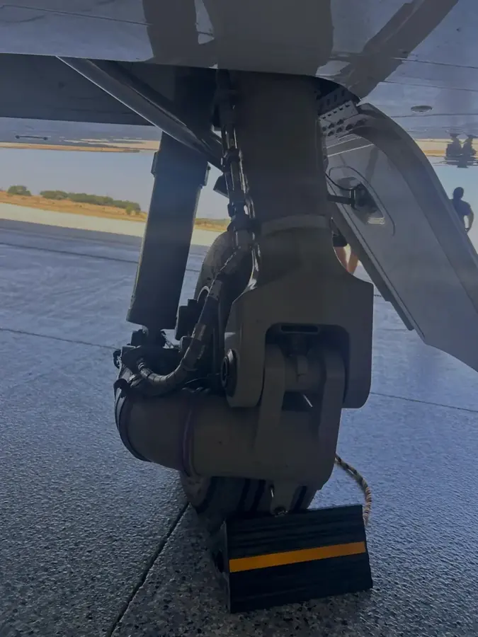 A main landing gear leg close up showing the brake assembly, tire, hydraulic lines and a wheel chock.