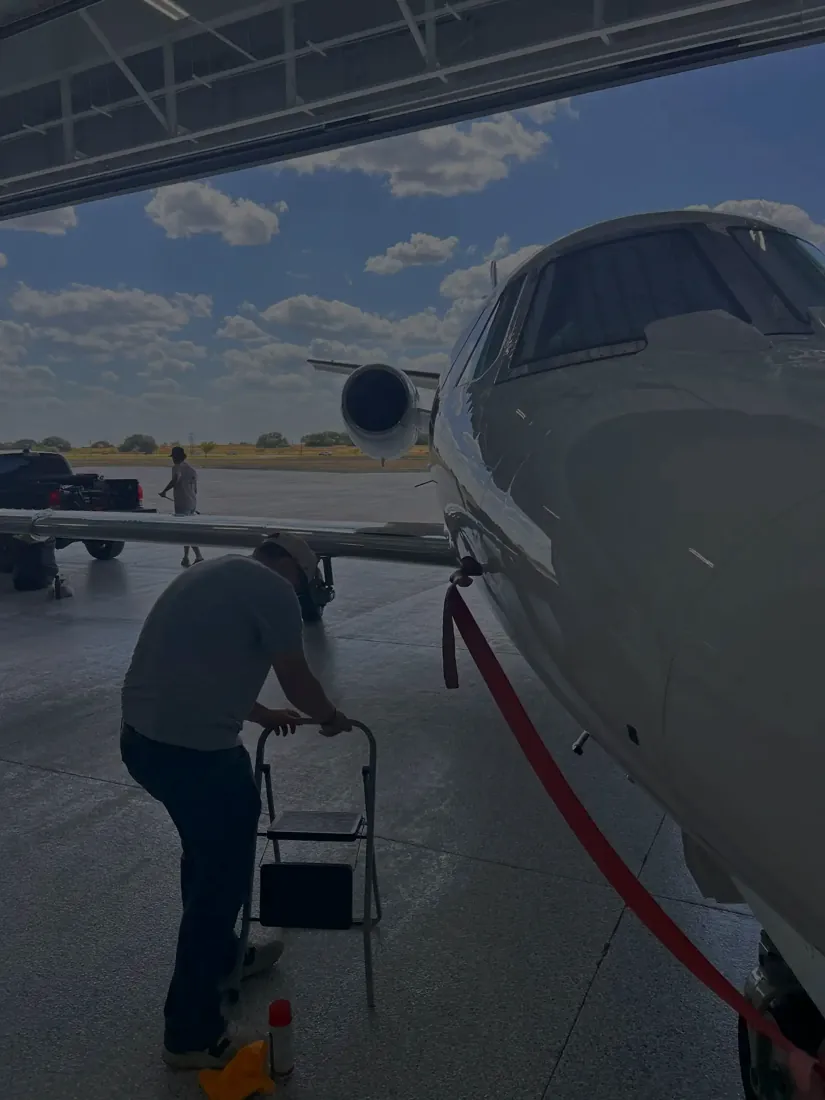 Somebody working beside the nose of a business jet from a step stool, in a hangar.