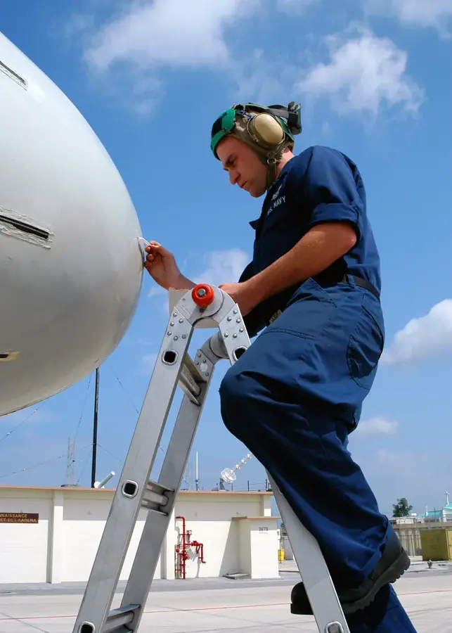 A technician on a ladder working on the white nose radome of an aircraft.