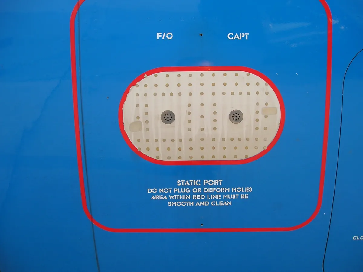 A static port on a fuselage, a perforated plate ringed by a red line, with a placard reading DO NOT PLUG OR DEFORM HOLES, AREA WITHIN RED LINE MUST BE SMOOTH AND CLEAN.