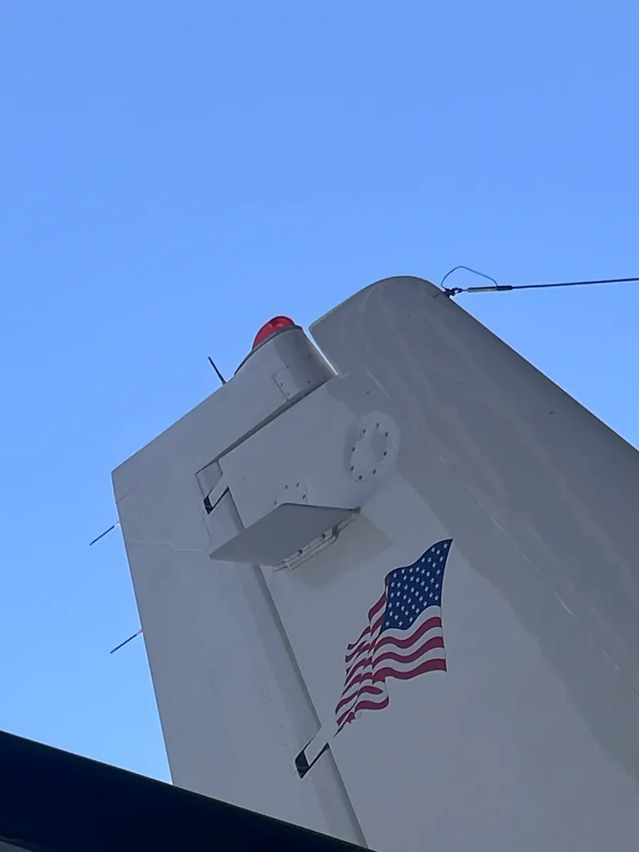 The top of a vertical fin against blue sky with thin black static wicks projecting from the trailing edge.